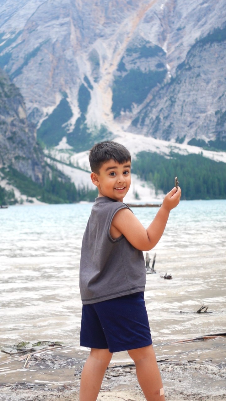 A child smiling toward the camera beside a mountain lake